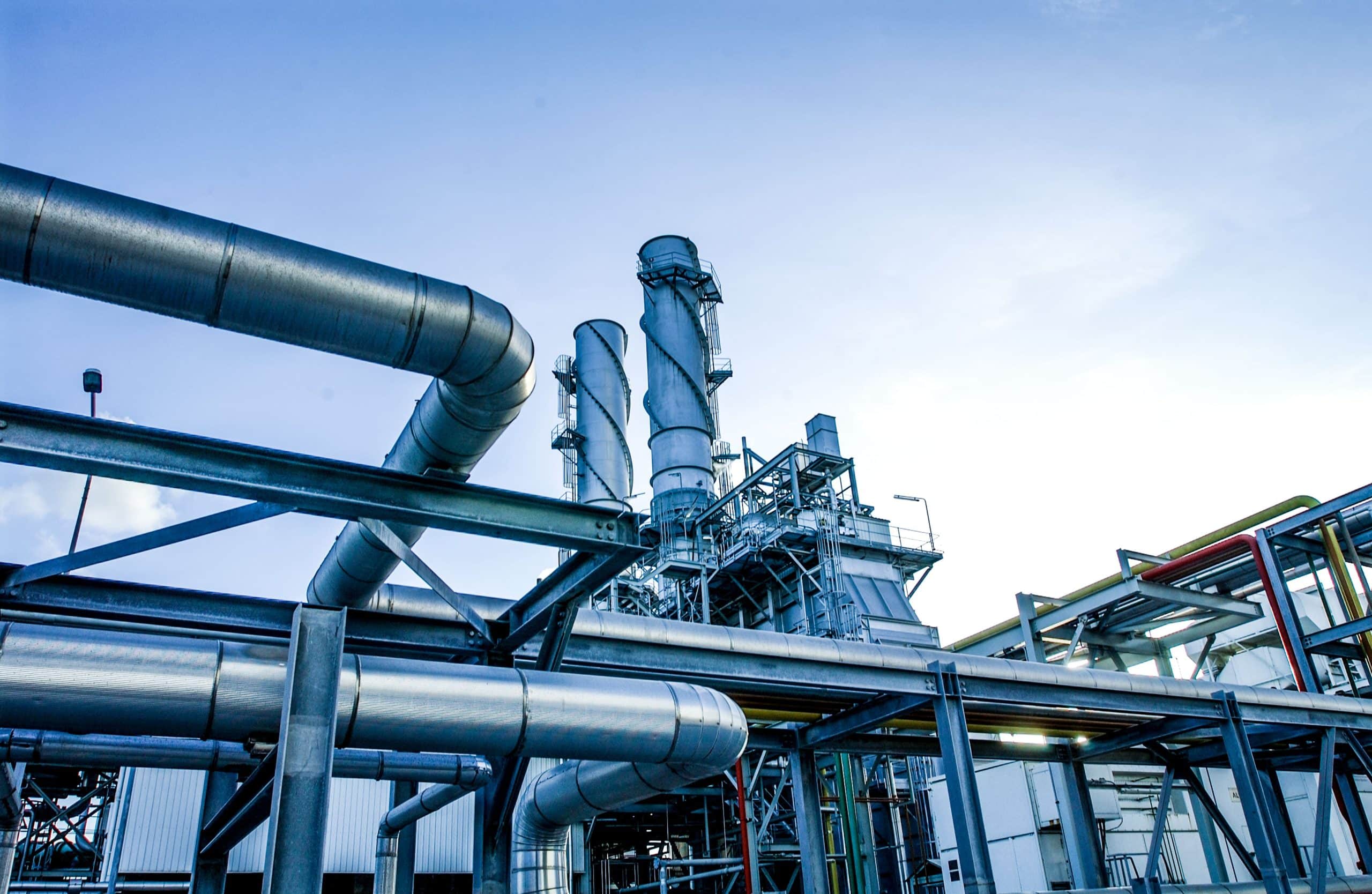 IndustrialMarket Industrial plant with large metal pipes and chimneys against a clear blue sky.