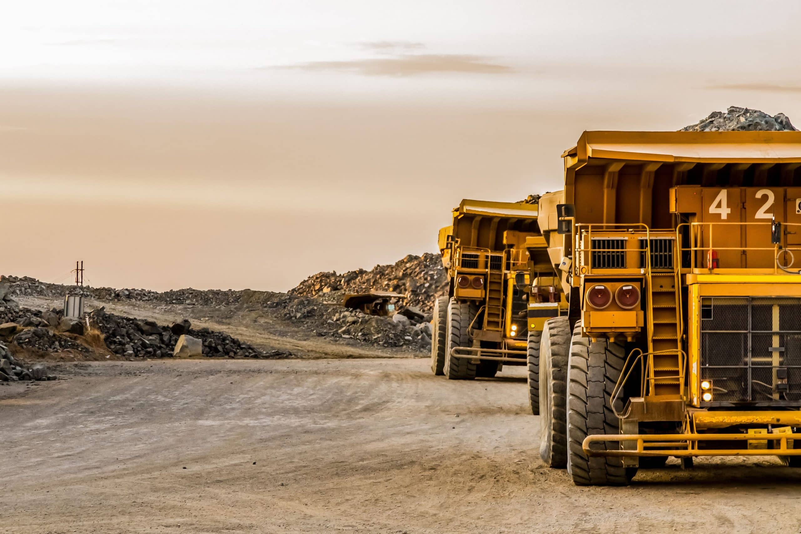 AdobeStock_194464715 (1) Two large yellow trucks moving across a rocky terrain