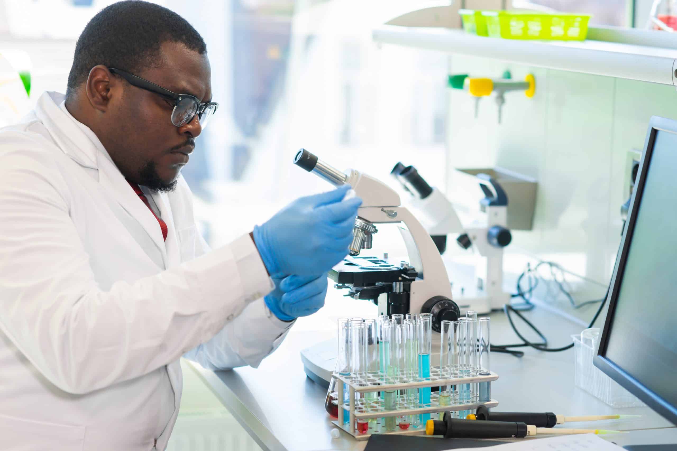 African-american medical doctor working in research lab. Science assistant making pharmaceutical experiments. Chemistry, medicine, biochemistry, biotechnology and healthcare concept. Scientist wearing goggles and gloves using a pipette with yellow liquid in a lab.