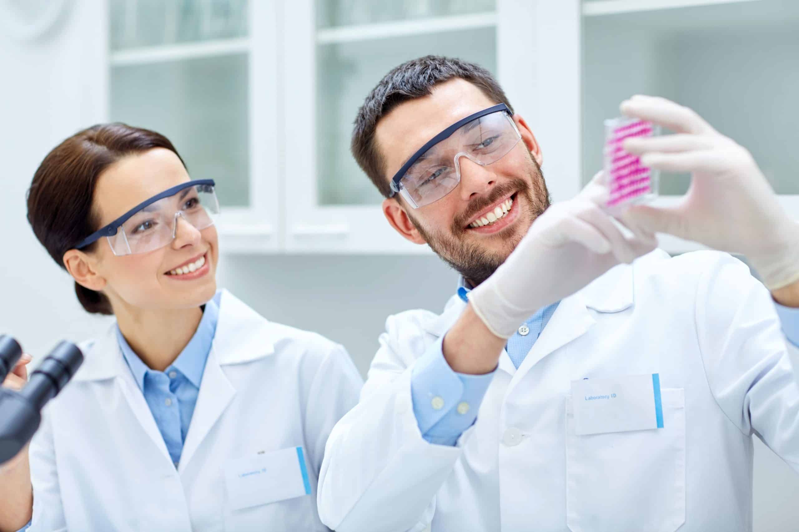 OurExpertise Two lab scientists smiling while viewing a strip with pinks dots